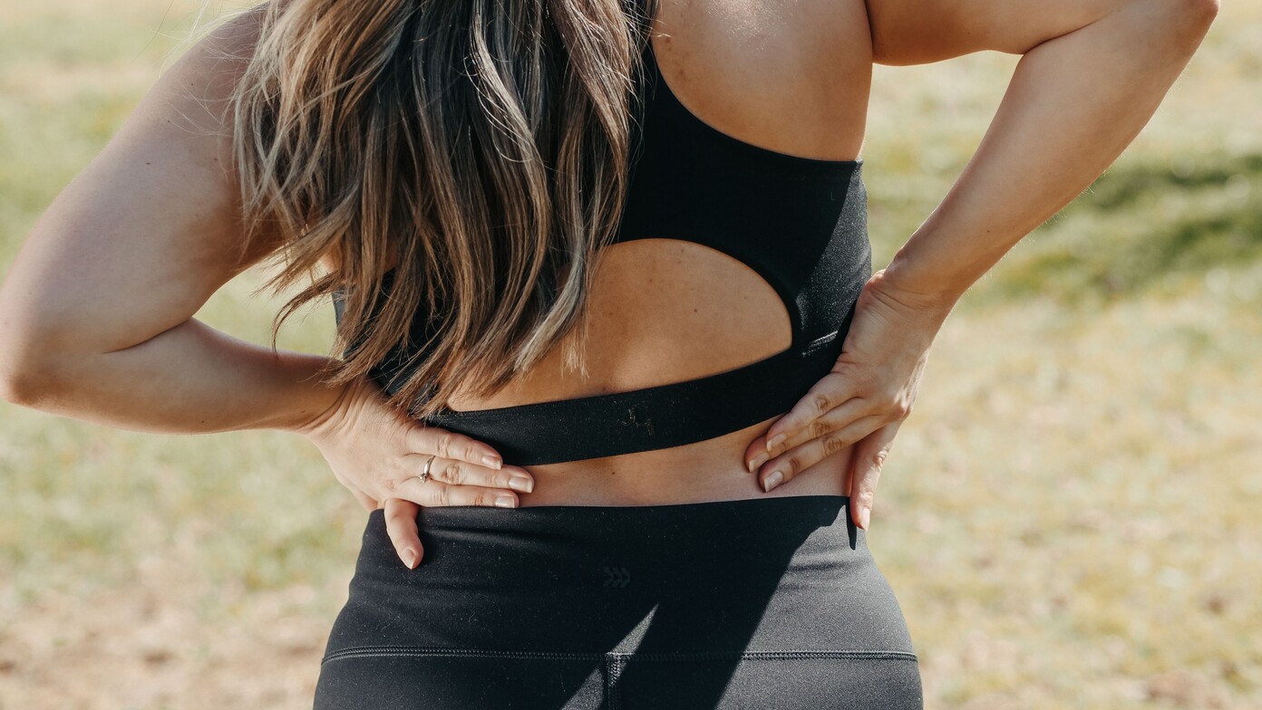 A close up of a woman holding her lower back in pain