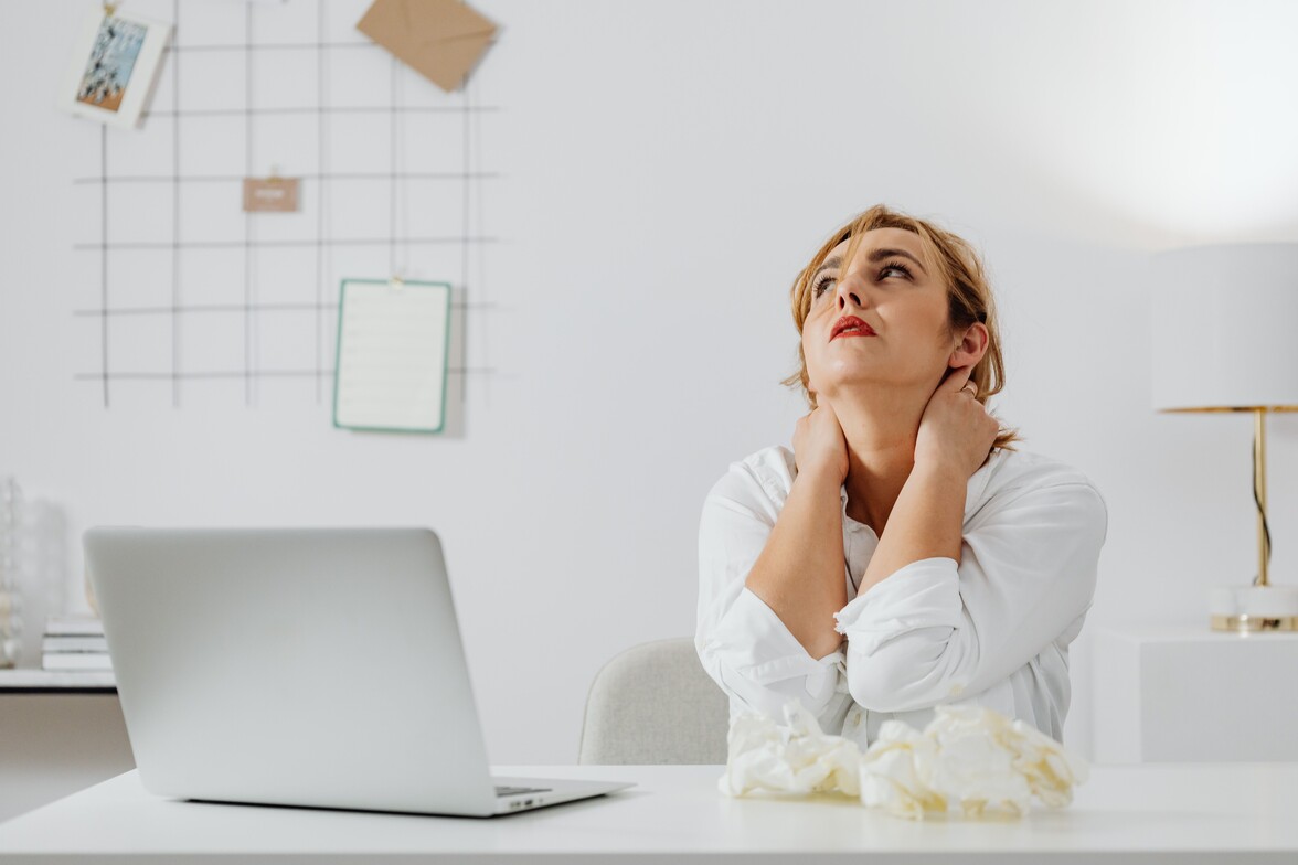 A woman holding her neck in pain after a car accident sitting sown at a desk with a laptop