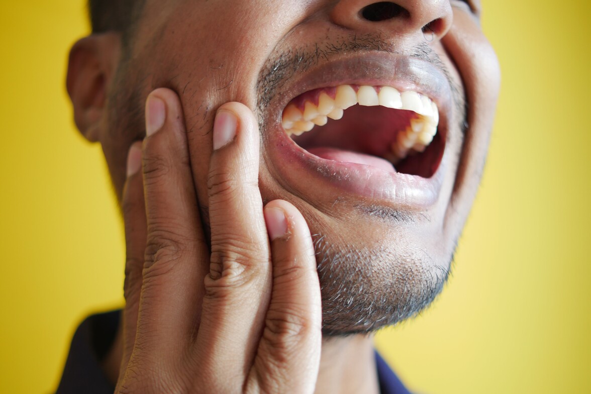 MAN HOLDS HIS JAW IN PAIN FROM TMJ DISORDER